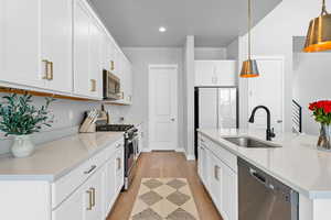 Kitchen with decorative light fixtures, stainless steel appliances, light countertops, white cabinetry, and a sink