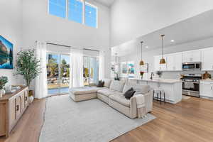 Living area featuring light wood-type flooring, a towering ceiling, an inviting chandelier, and recessed lighting