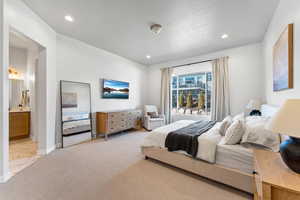 Bedroom featuring a textured ceiling, connected bathroom, recessed lighting, light colored carpet, and baseboards