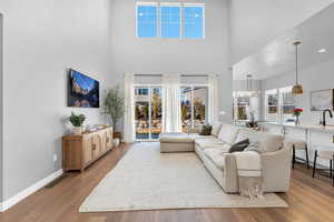 Living room featuring light wood-type flooring, visible vents, a towering ceiling, and baseboards