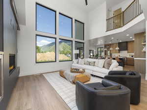 Living room with light wood-type flooring, a large fireplace, a towering ceiling, and baseboards