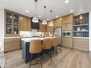 Kitchen with a sink, light countertops, appliances with stainless steel finishes, glass insert cabinets, and pendant lighting