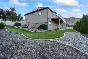 Rear view of property featuring a fenced backyard, solar panels, stone siding, a lawn, and stucco siding