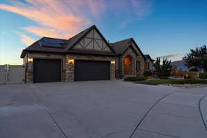 Tudor-style house featuring a garage, solar panels, concrete driveway, a gate, and stucco siding