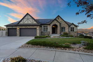 Tudor-style house with a garage, solar panels, a yard, concrete driveway, and stucco siding