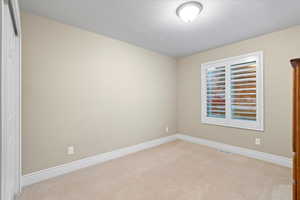 Spare room with light colored carpet, visible vents, a textured ceiling, and baseboards