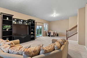 Living area featuring stairs, baseboards, a textured ceiling, and light colored carpet