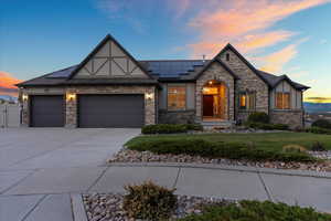 English style home with a garage, concrete driveway, stucco siding, and roof mounted solar panels