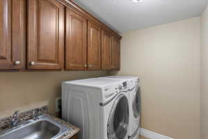 Laundry area featuring cabinet space, baseboards, a textured ceiling, washing machine and dryer, and a sink