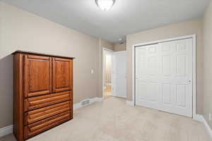 Bedroom featuring a closet, light colored carpet, visible vents, a textured ceiling, and baseboards