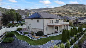 Back of house featuring solar panels, a mountain view, a balcony, stone siding, and a fenced backyard