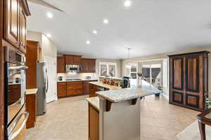 Kitchen with a spacious island, light stone counters, a breakfast bar, stainless steel appliances, and pendant lighting