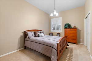 Bedroom featuring light carpet, vaulted ceiling, a chandelier, and baseboards