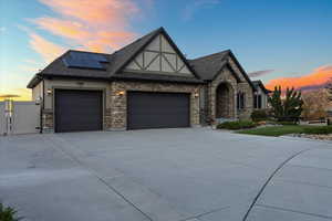 Tudor-style house featuring concrete driveway, solar panels, an attached garage, a gate, and stucco siding