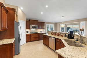 Kitchen featuring appliances with stainless steel finishes, hanging light fixtures, light stone countertops, a sink, and backsplash