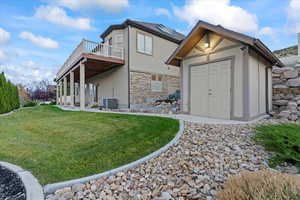 Back of house with an outbuilding, a deck, a yard, stone siding, and stucco siding