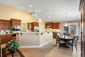 Kitchen with stainless steel appliances, a kitchen breakfast bar, light stone countertops, a center island with sink, and pendant lighting
