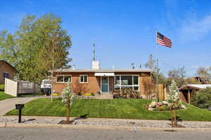 Ranch-style home with brick siding, a chimney, concrete driveway, fence, and a front lawn