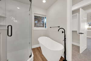 Bathroom featuring a freestanding bath, a stall shower, wood finished floors, and baseboards