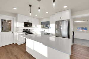 Kitchen with hanging light fixtures, appliances with stainless steel finishes, dark wood-style flooring, and white cabinetry