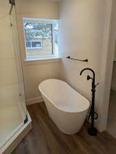 Bathroom featuring a soaking tub, baseboards, a shower with door, and wood finished floors