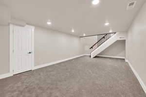 Finished basement featuring visible vents, stairway, and carpet flooring