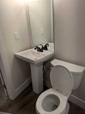 Bathroom featuring toilet, a sink, baseboards, and wood finished floors