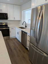 Kitchen with light stone counters, appliances with stainless steel finishes, dark wood-type flooring, white cabinetry, and a sink