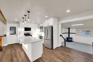 Kitchen featuring a sink, white cabinetry, light countertops, appliances with stainless steel finishes, and a wood stove