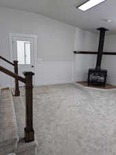 Unfurnished living room featuring a wood stove, stairs, light carpet, and a textured ceiling