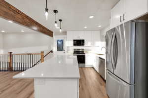 Kitchen featuring appliances with stainless steel finishes, light wood-style floors, a sink, a kitchen island, and beamed ceiling