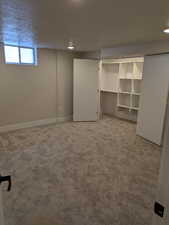 Below grade area with light carpet, a textured ceiling, and baseboards