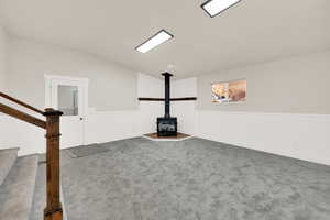 Interior space featuring a wood stove, stairs, vaulted ceiling, and dark colored carpet