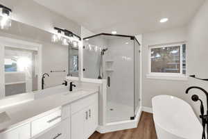 Bathroom with a stall shower, a soaking tub, vanity, and wood finished floors