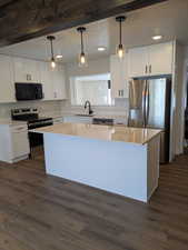 Kitchen featuring stainless steel appliances, a center island, white cabinetry, and hanging light fixtures