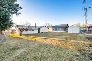 Back of property with a shed, a lawn, an outdoor structure, and fence