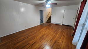 Empty room with dark wood-type flooring, visible vents, stairway, and a ceiling fan