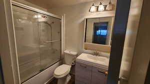 Bathroom with vanity, toilet, and bath / shower combo with glass door