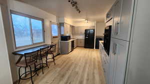 Kitchen with gray cabinets, light countertops, track lighting, light wood-type flooring, and black appliances