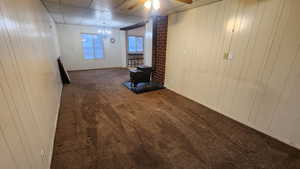 Unfurnished living room with a drop ceiling, ceiling fan with notable chandelier, wood walls, carpet flooring, and a wood stove