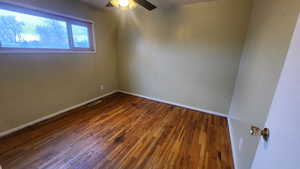 Spare room with dark wood-style floors, visible vents, baseboards, and a ceiling fan