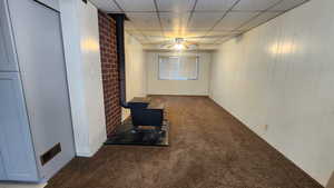 Interior space with visible vents, a ceiling fan, brick wall, a wood stove, and a paneled ceiling