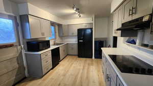 Kitchen with light countertops, gray cabinetry, a sink, under cabinet range hood, and black appliances