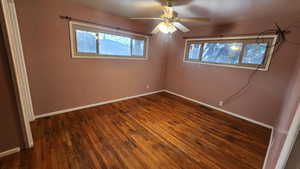 Unfurnished bedroom featuring a ceiling fan, multiple windows, baseboards, and dark wood-type flooring