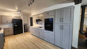 Kitchen featuring gray cabinetry, light countertops, under cabinet range hood, and black appliances