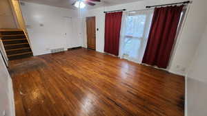 Unfurnished room featuring ceiling fan, visible vents, baseboards, stairway, and dark wood-style floors