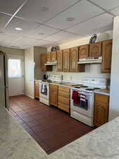 Kitchen with freestanding refrigerator, dark tile patterned floors, under cabinet range hood, and white range with electric cooktop