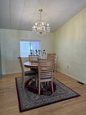 Dining area featuring a notable chandelier, light wood finished floors, visible vents, a decorative wall, and a textured ceiling