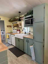 Kitchen with pendant lighting, white appliances, a sink, and wooden counters