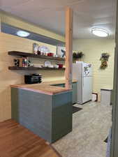 Kitchen with open shelves, wood walls, light wood-type flooring, and freestanding refrigerator